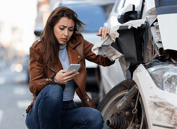 Woman on her cell phone and kneeling beside her car that has been in a bad wreck
