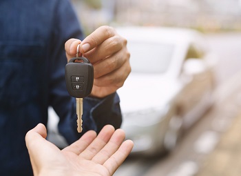 person handing over car keys to a rental car parked in the background