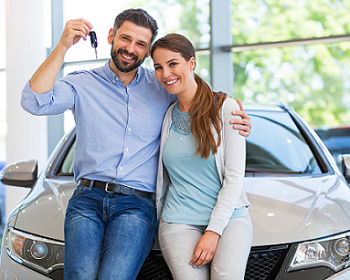 Couple posing in from of new car at dealership the man has a car key held up in his hand and his other arm around his wife