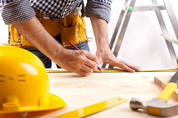 contractor marking a piece of wood next to a yellow hard hat